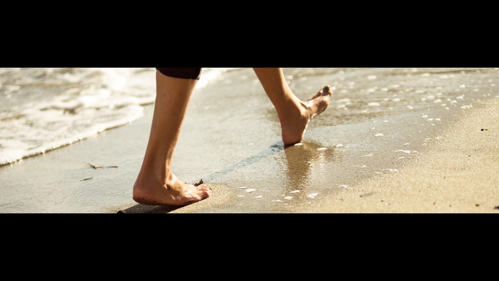 Blote benen en voeten, wandelend over het strand, dichtbij de branding.