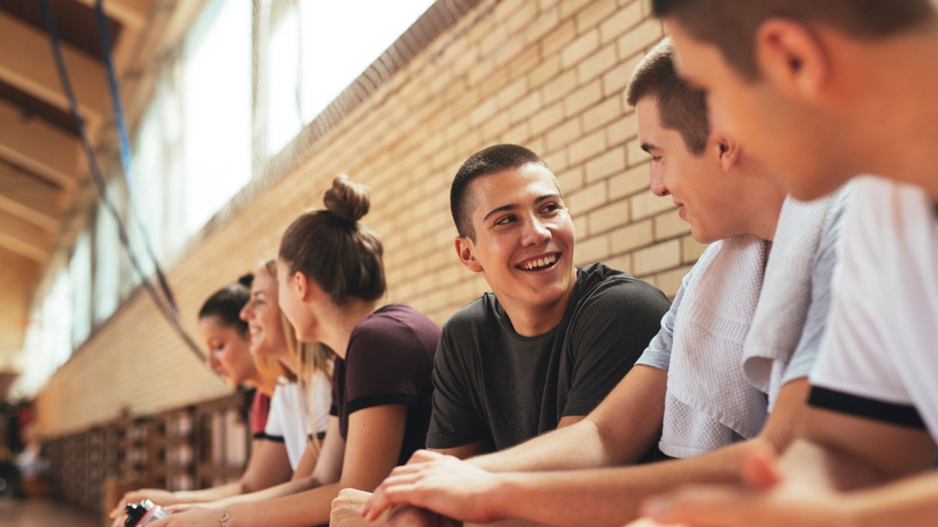 Lachende jonge man zittend op bank in sporthal